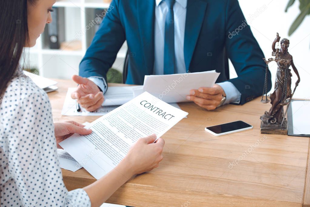 cropped shot of lawyer holding papers and client reading contract in office