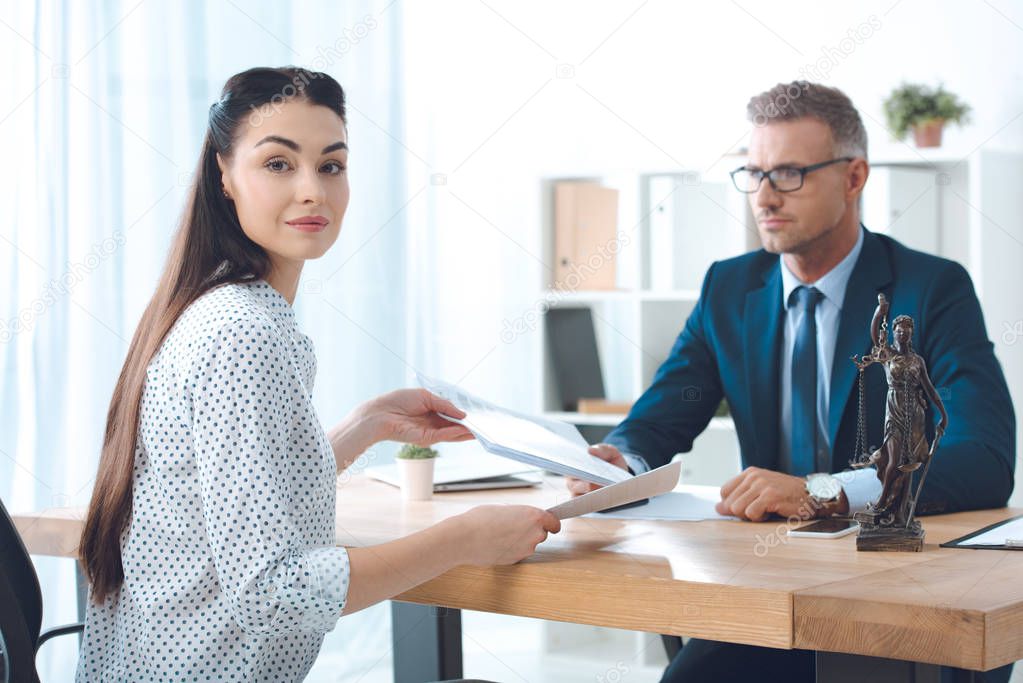 young woman smiling at camera while sitting with lawyer in office