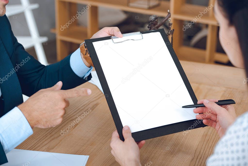 cropped shot of lawyer pointing clipboard and woman signing paper