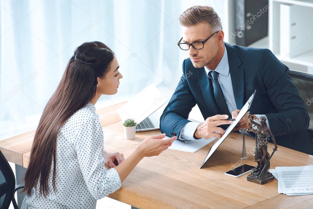 male lawyer pointing at clipboard and looking at client in office