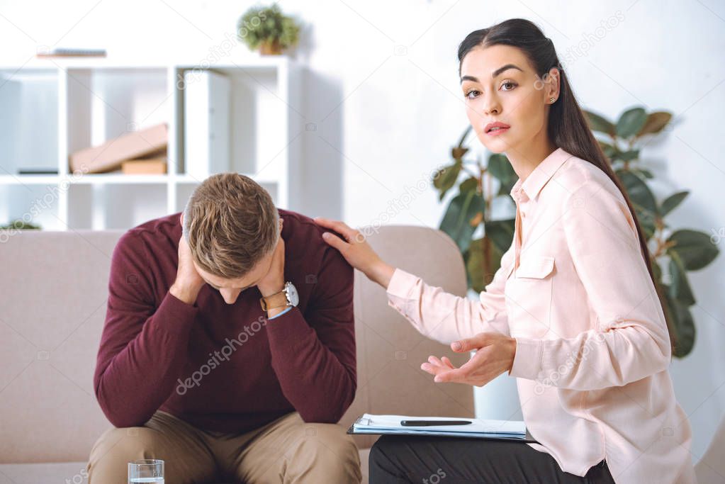 psychotherapist looking at camera while supporting upset patient in office
