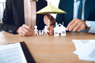 partial view of insurance agents covering family and house paper models with umbrella at workplace clipart