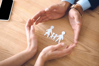 partial view of insurance agents and female hands with family paper model on wooden tabletop, family insurance concept clipart