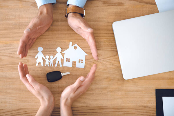 partial view of insurance agents and female hands with house, family paper models and car key on wooden tabletop