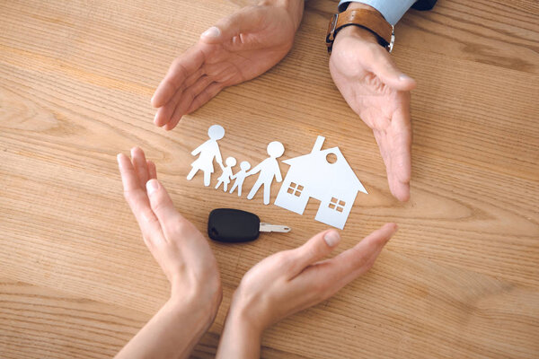 partial view of insurance agents and female hands with house, family paper models and car key on wooden tabletop