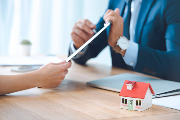 обрезанный снимок страхового агента, указывающего на буфер обмена в руках клиентов за столом в офисе, концепция страхования дома
