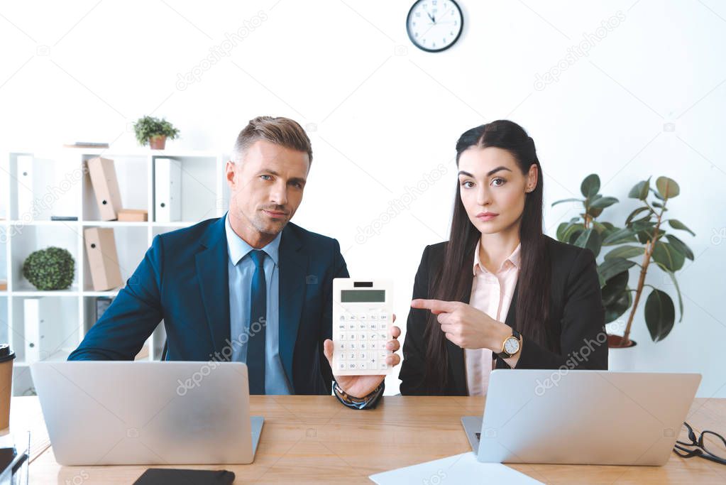 portrait of businesswoman pointing at calculator in colleagues hand at workplace in office