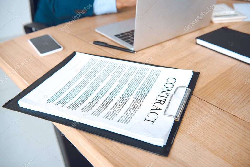 cropped shot of businessman at workplace with laptop and contract in office