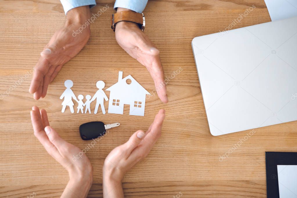 partial view of insurance agents and female hands with house, family paper models and car key on wooden tabletop
