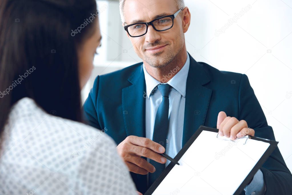 insurance agent pointing at clipboard in clients hand at tabletop in office