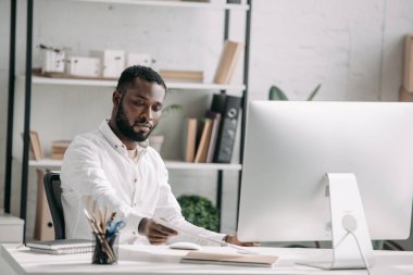 bilgisayar ve tablo Office belgelerinden alarak çalışan yakışıklı Afrikalı-Amerikalı iş adamı