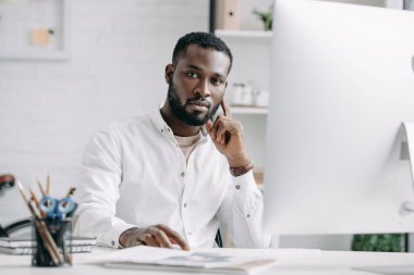 bilgisayarda Office çalışan ve kameraya bakarak ciddi yakışıklı Afrikalı-Amerikalı işadamı