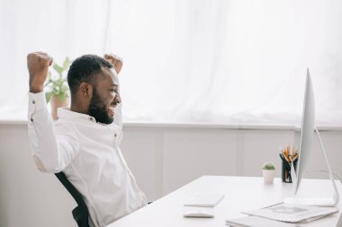 bilgisayarda Office çalışan ve Evet jest gösterilen mutlu Afrika kökenli Amerikalı işadamı yan görünüm