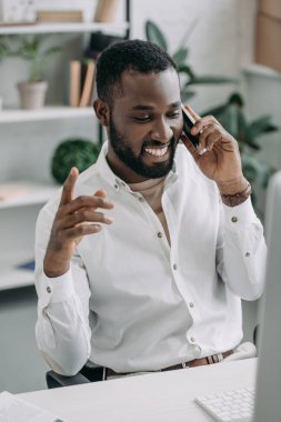 Smartphone ile konuşmak ve ofiste mimik neşeli yakışıklı Afrikalı-Amerikalı işadamı