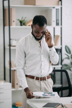 yakışıklı Afrikalı-Amerikalı işadamı smartphone ofiste tarafından konuşmak ve gazete okuma