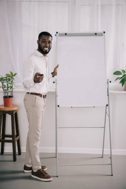 Flipchart duran ve ofiste mimik gülümseyen yakışıklı Afrikalı-Amerikalı işadamı