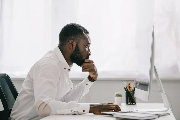 英俊的非洲裔美国商人的侧视图在手上休息下巴和工作在计算机在办公室 — 图库照片