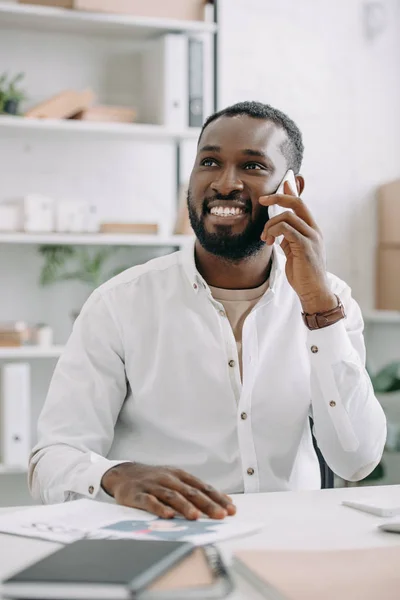 ハンサムなアフリカ系アメリカ人のビジネスマンと見上げるとオフィスでスマート フォンで話を笑ってください  — 無料ストックフォト