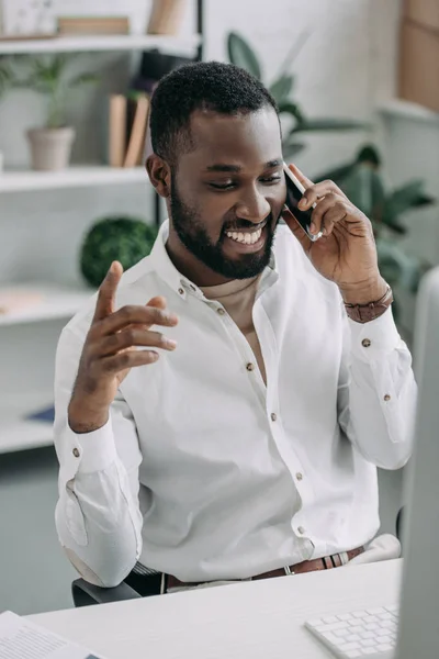 Веселый Красивый Африканский Бизнесмен Разговаривающий Смартфону Жестикулирующий Офисе — Бесплатное стоковое фото