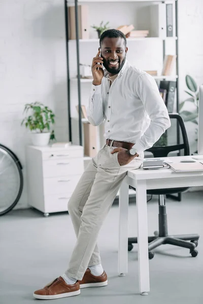 Красивый Африканский Американский Бизнесмен Опираясь Стол Разговаривая Смартфону Офисе — Бесплатное стоковое фото