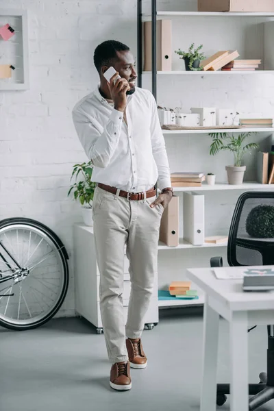 英俊的非洲裔美国商人交谈的智能手机在办公室和看远 — 免费的图库照片