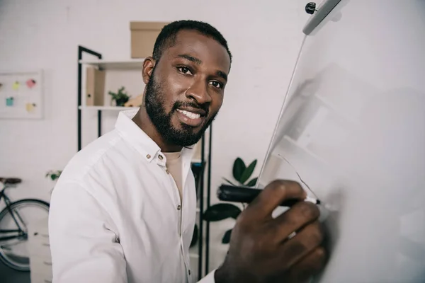 Sorrindo Bonito Empresário Afro Americano Desenhando Flipchart Escritório Olhando Para — Fotografia de Stock