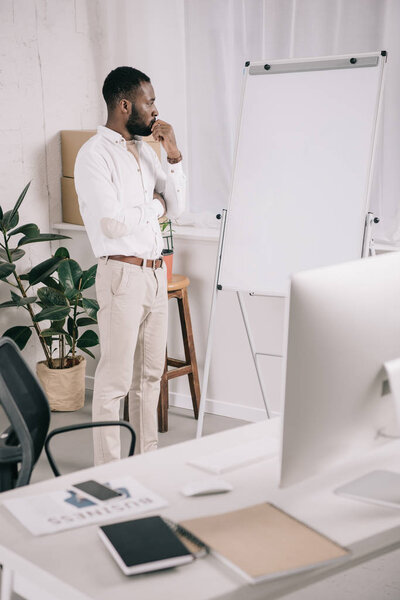 красивый задумчивый африканский бизнесмен смотрит на флипчарт в офисе

