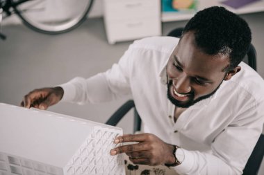 yakışıklı Afrikalı-Amerikalı mimar mimari ofis modelinde bakarak gülen, yüksek açılı görünüş
