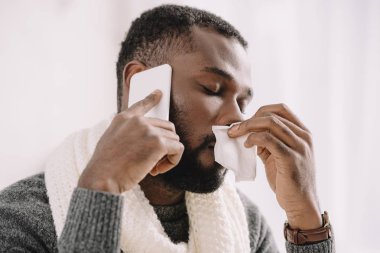 peçete smartphone üzerinde konuşurken tutan burun akıntısı olan hastalıklı Afrikalı-Amerikalı adam
