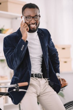 Afrika kökenli Amerikalı işadamı smartphone üzerinde bisiklet Office yaslanmış iken konuşmak gülümseyen