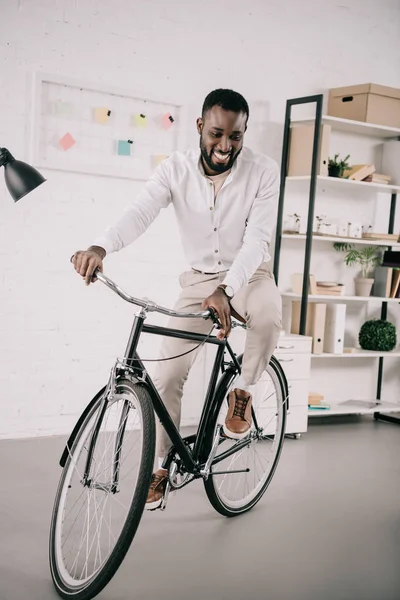 オフィスでハンサムなアフリカ系アメリカ人実業家乗って自転車を笑顔  — 無料ストックフォト