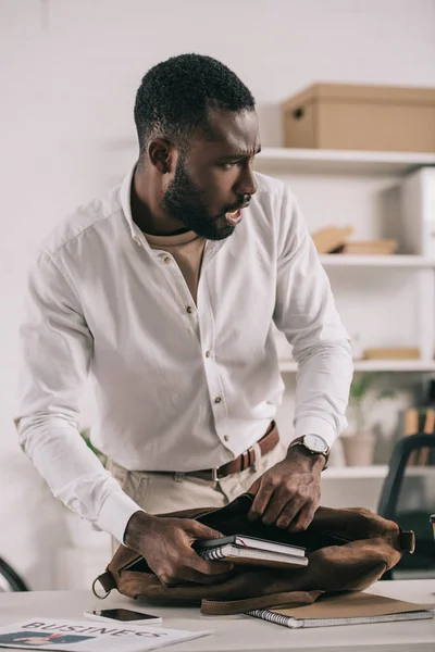 Shocked Handsome African American Businessman Putting Notebooks Briefcase Looking Away — Free Stock Photo