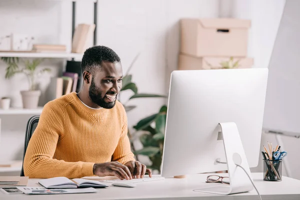 사무실에서 컴퓨터에서 주황색 스웨터에 잘생긴 아프리카계 미국인 디자이너 — 스톡 사진