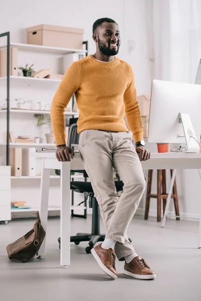 Усміхнений Красивий Афроамериканський Дизайнер Помаранчевому Светрі Спираючись Стіл Дивлячись Офіс — стокове фото
