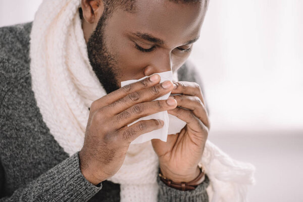 ill african american man with runny nose holding napkin