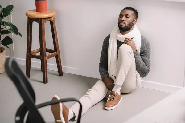 diseased african american man in warm scarf sitting on floor in office