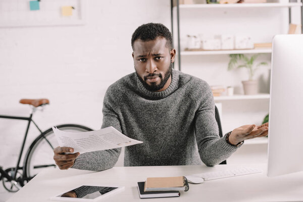 confused bearded african american businessman with shrug gesture holding document in office 