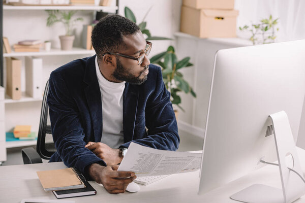 бородатый африканский американский бизнесмен делает бумажную работу в офисе с компьютером
