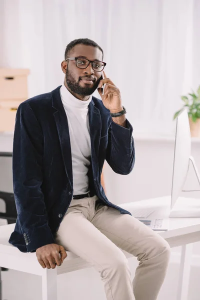 Knappe Afro Amerikaanse Zakenman Praten Smartphone Terwijl Zittend Tafel — Gratis stockfoto