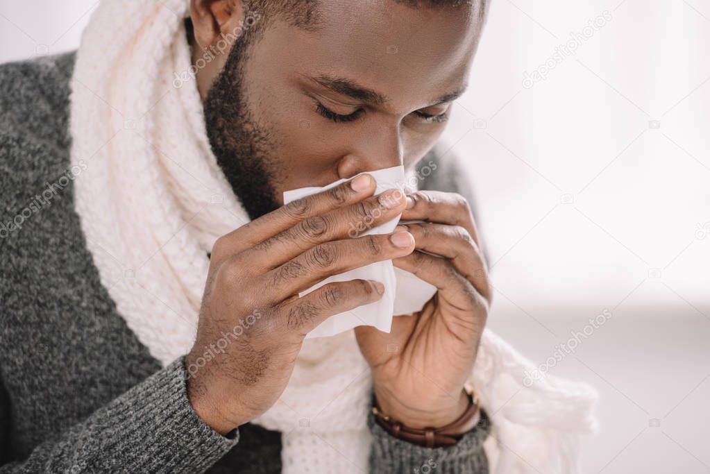 ill african american man with runny nose holding napkin