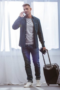 pasaportu taşıyan ile yetişkin erkek yolcunun tekerlekli çanta ve Smartphone'da evde konuşmak 