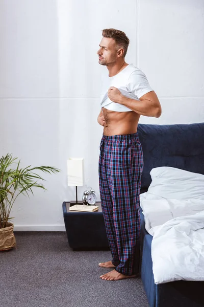 Hombre Adulto Poniéndose Una Camiseta Blanca Cerca Cama Casa — Foto de Stock