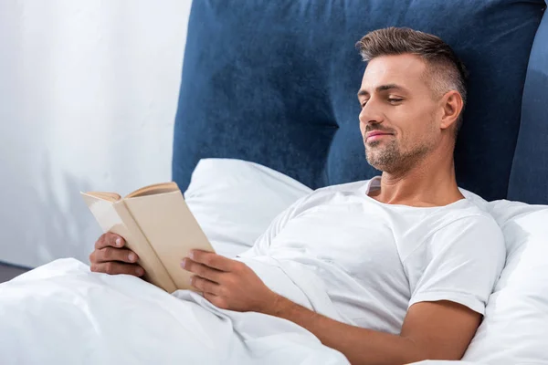 Homem Sorrindo Livro Leitura Enquanto Deitado Cama Durante Manhã Casa — Fotografia de Stock