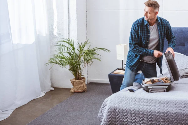 Smiling Male Traveler Packing Luggage Looking Away Bedroom Home — Stock Photo, Image