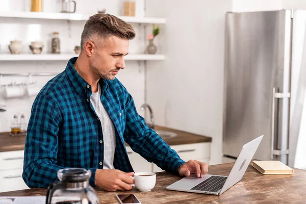 Homem Bonito Camisa Quadriculada Segurando Xícara Café Usando Laptop Casa — Fotos gratuitas