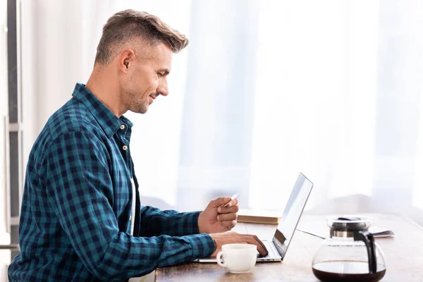 Vista Lateral Homem Sorridente Segurando Cartão Crédito Usando Laptop Casa — Fotografia de Stock