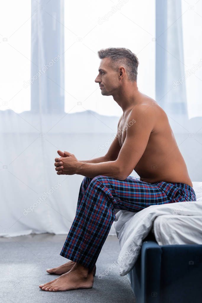 side view of shirtless man sitting on bed during morning time at home