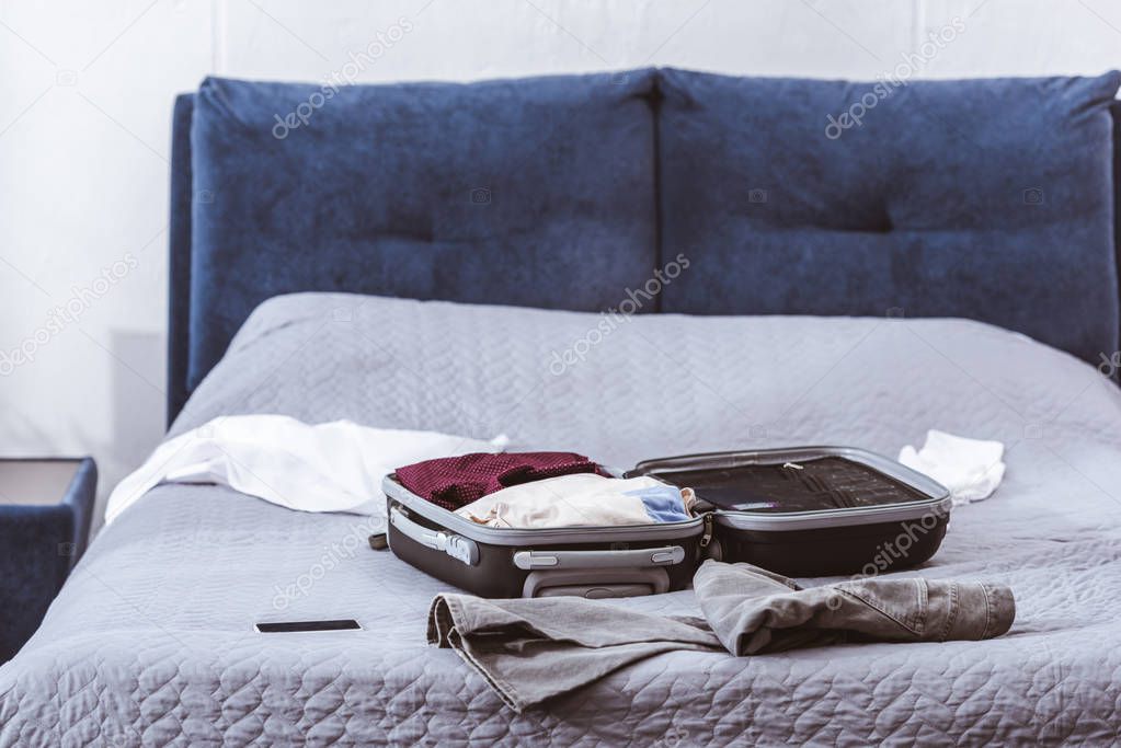 selective focus of travel bag, clothes and smartphone on bed at home 