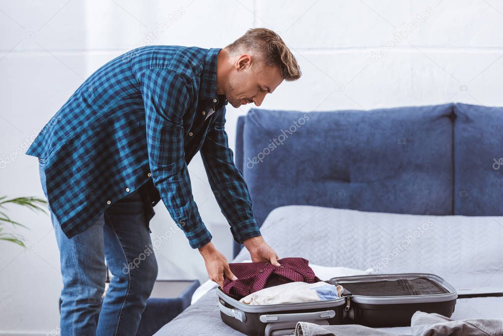 side view of male traveler packing luggage in bedroom at home 