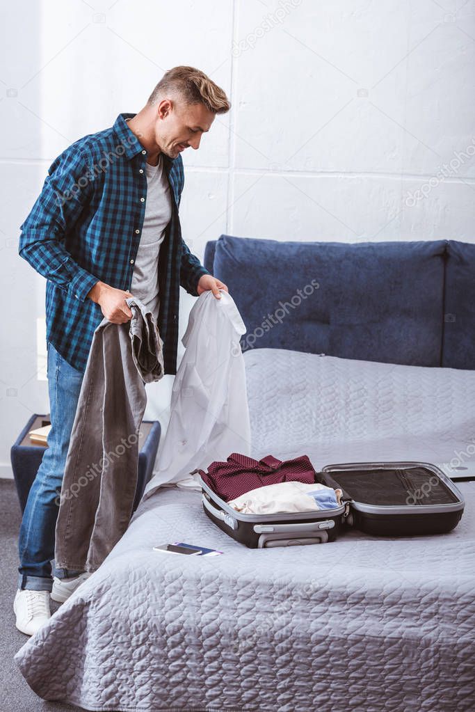 handsome adult male traveler packing luggage in bedroom at home 